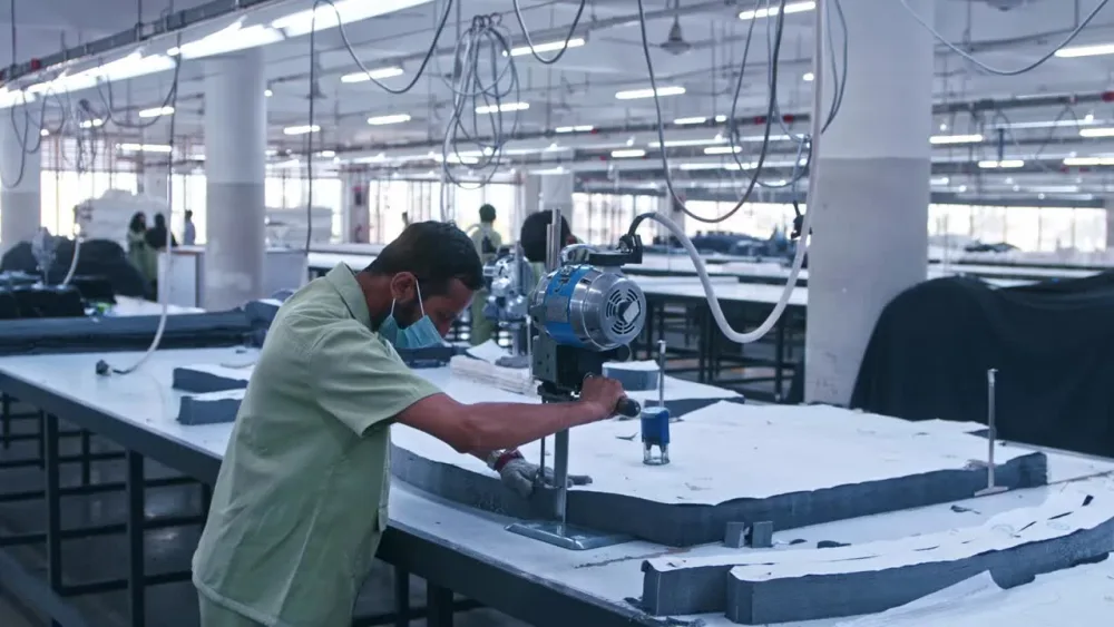Pattern pieces being cut from layered denim on a factory table
